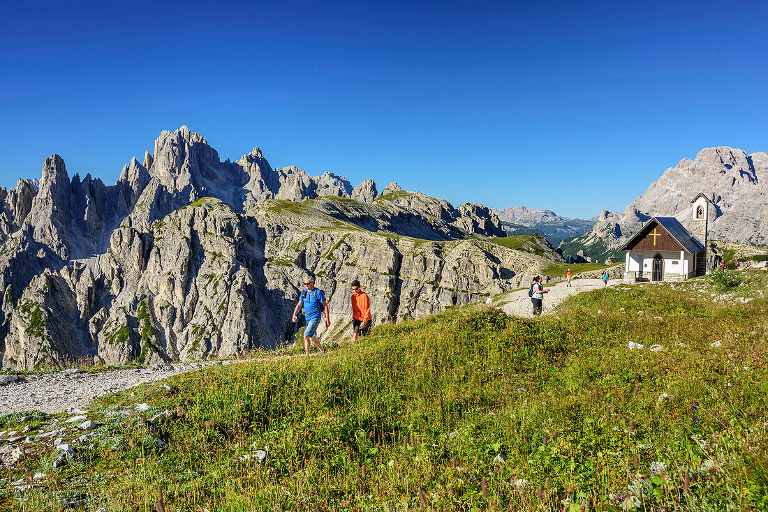 Mehrere Personen wandern an Kapelle vorbei, Cadinigruppe im Hintergrund, Paternsattel, Sextener Dolomiten, Dolomiten, UNESCO Weltnaturerbe Dolomiten, Südtirol, Italien