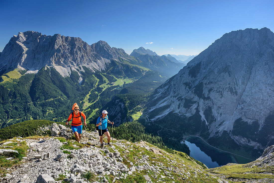 Man and woman hiking towards Ehrwalder Sonnenspitze, Wetterstein range with Zugspitze and lake Seebensee in background, Ehrwalder Sonnenspitze, Mieming range, Tyrol, Austria