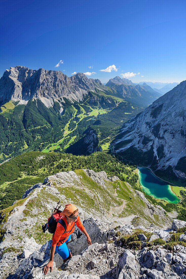 Woman hiking towards Ehrwalder Sonnenspitze, Wetterstein range with Zugspitze and lake Seebensee in background, Ehrwalder Sonnenspitze, Mieming range, Tyrol, Austria