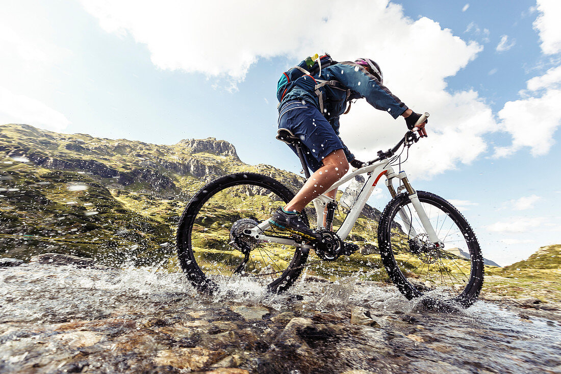 Mountainbikerin spritzt durch Gebirgsbach am Giglachsee, Niedere Tauern, Steiermark, Österreich