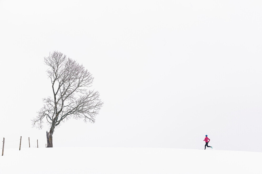 Junge Frau joggt durch verschneite Landschaft in Berg am Starnberger See, Bayern, Deutschland.