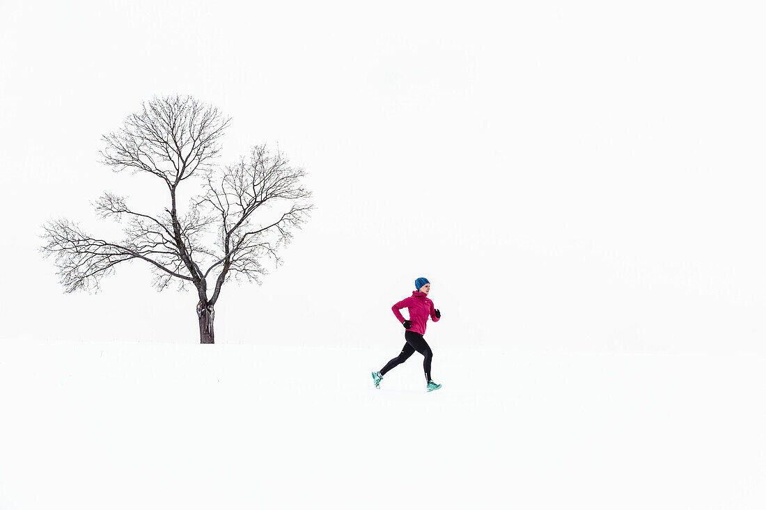 Junge Frau joggt durch verschneite Landschaft in Berg am Starnberger See, Bayern, Deutschland.