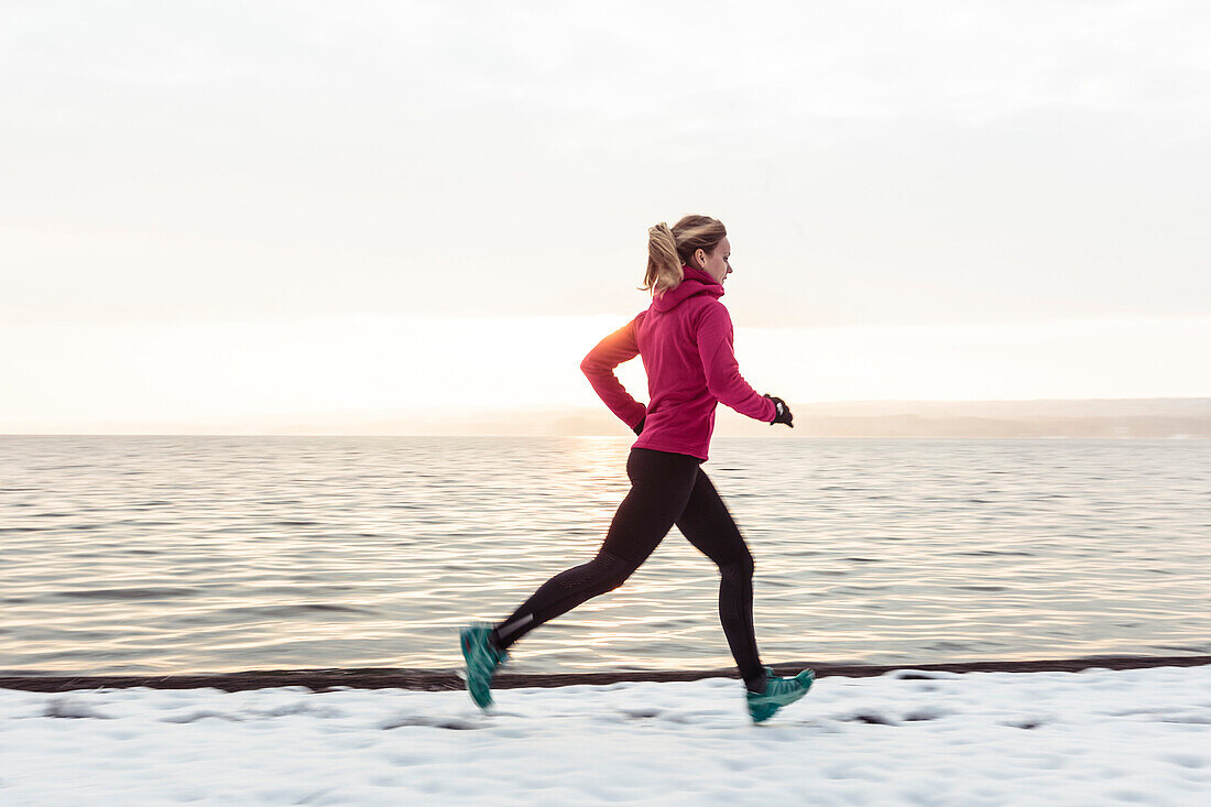 Junge Frau joggt am verschneiten Starnberger See, Bayern, Deutschland.