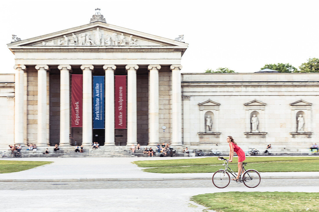 Junge Frau radelt vor Glyptothek am Königsplatz in München, Bayern, Deutschland