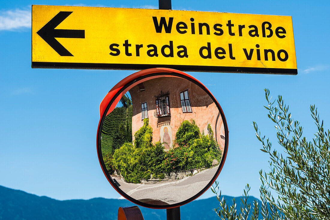 An old house reflected in a mirror beneath the wine route sign, Magreid, South Tyrol, Italy
