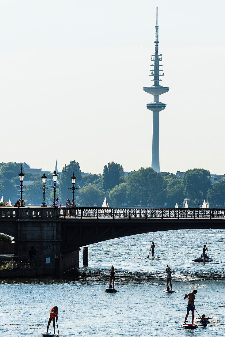 Stand up canoeist on lake Aussenalster in front of Schwanenwik bridge, Hamburg, Germany