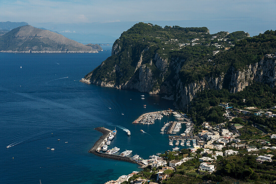 The rugged cliffs along the coastline of the island of Capri, and the town of Capri with a harbour, Capri, Campania, Italy