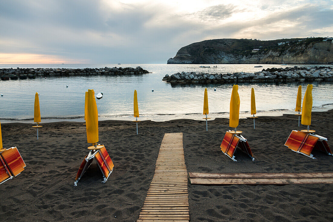 Wooden boardwalk and yellow umbrellas on the beach of Sant Angelo, Sant Angelo, Ischia, Campania, Italy