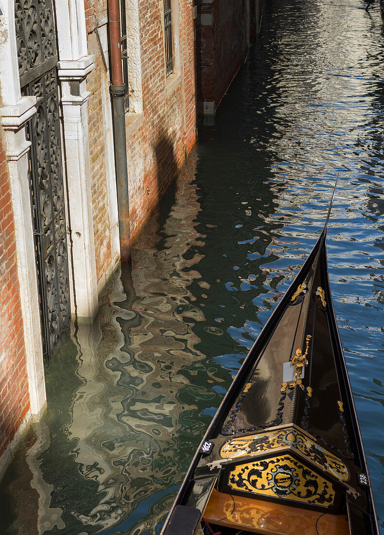 Bow of a gondola in a canal beside a brick wall, Venice, Italy