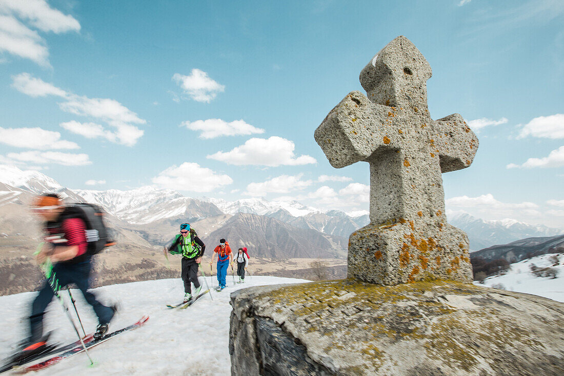 Eine Gruppe von Skifahrern läuft an einem Steinkreuz in den Bergen vorbei, Gudauri, Mzcheta-Mtianeti, Georgien