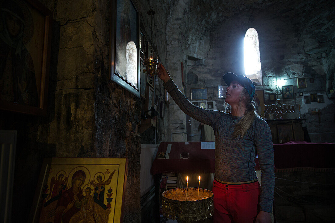 Young woman lighting a candle in a small church, Gudauri, Mtskheta-Mtianeti, Georgia