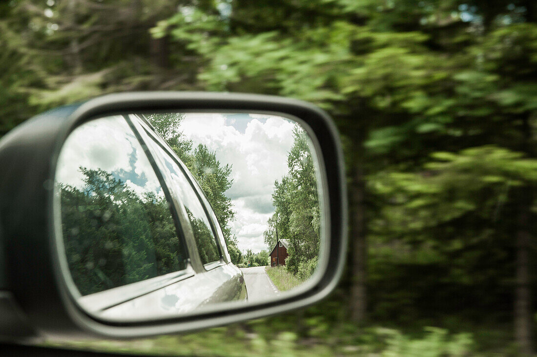 Blick in den Auto Außenspiegel auf eine Landstraße mit einem roten Holzhaus, Halland, Schweden
