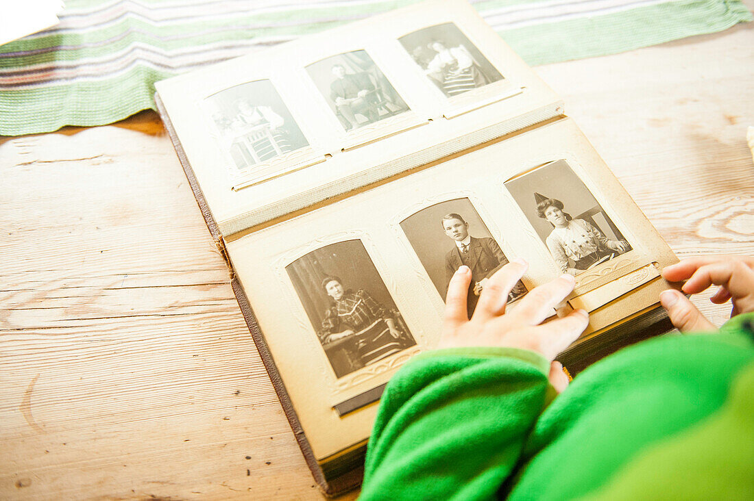 Kind blickt in ein Fotoalbum mit Fotografien aus alten Zeiten im Heimatmuseum Gammelgarden in Rättvik, Dalarna, Schweden