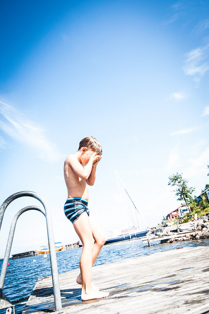 Junge steht nach dem Bad im Meer auf dem Bootssteg, Anskarsklubb, Öregrund, Uppsala, Schweden