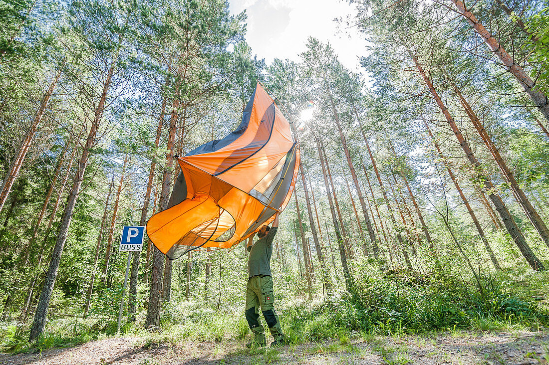 Mann schüttelt am Morgen sein Zelt aus im Wald von Trollegater, Kinda, Östergötland, Schweden