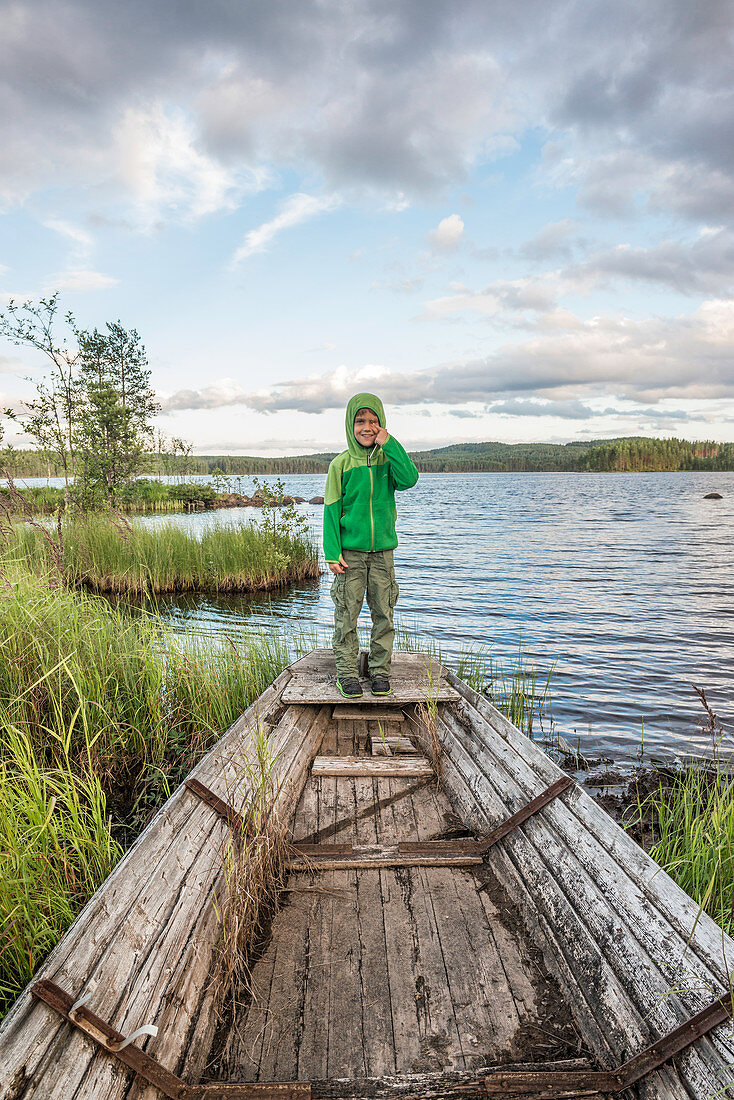 child standing on a rotten fishing boat on the shore of a small lake near Munkfors, Varmland, Sweden