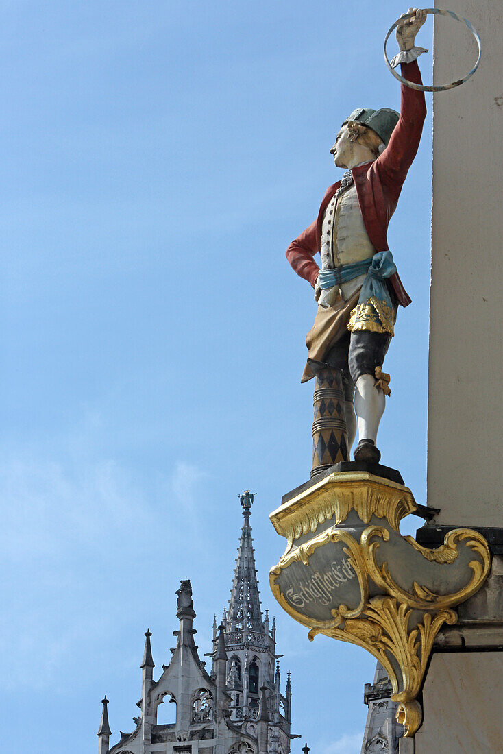 Statue of a Schaeffler at Schaefflereck with the steeple of Neues Rathaus, Munich, Bavaria, Germany