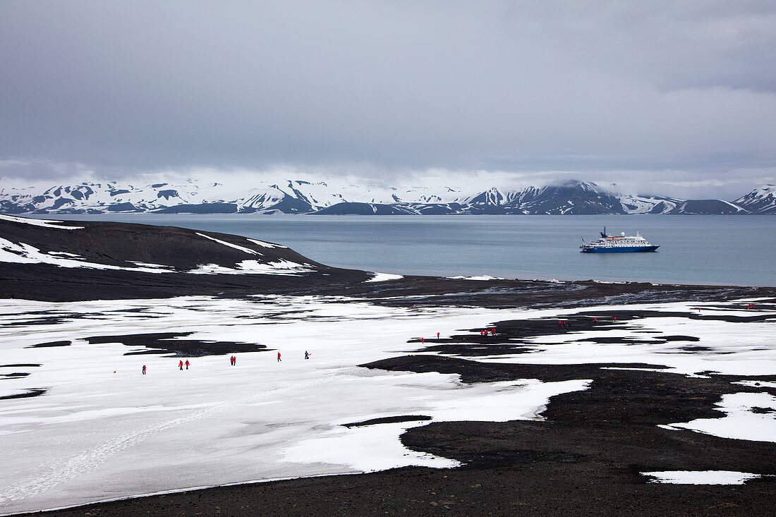 Passengers of expedition cruise ship MV Sea Spirit (Poseidon Expeditions) walk through snow-covered volcanic landscape Telefon Bay, Deception Island, South Shetland Islands, Antarctica