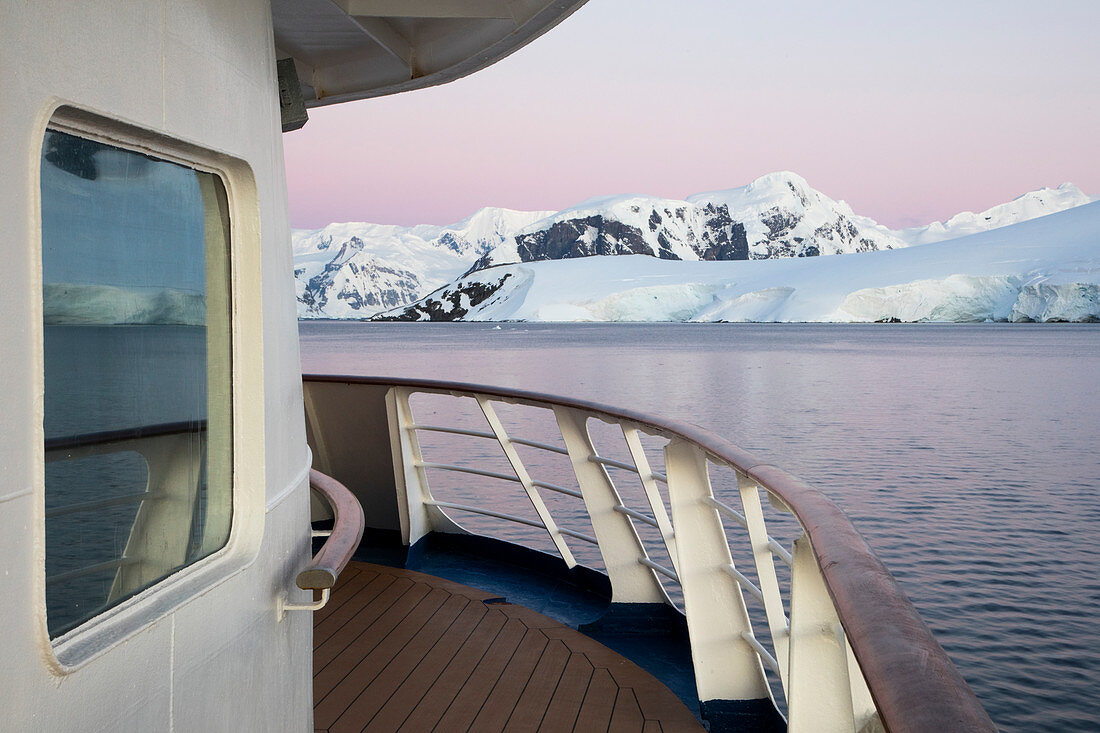 Deck von Expeditions Kreuzfahrtschiff MV Sea Spirit (Poseidon Expeditions) vor Eisberg und schneebedeckten Bergen in der Abenddämmerung. Paradise Harbor (Paradise Bay), Danco-Küste, Grahamland, Antarktische Halbinsel, Antarktis