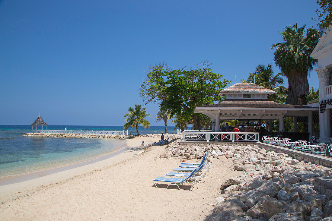 Strandliegen am Sunset Beach, die Cedar Bar und Steg mit Pavillon im Half Moon Resort, Rose Hall, nahe Montego Bay, Saint James, Jamaika