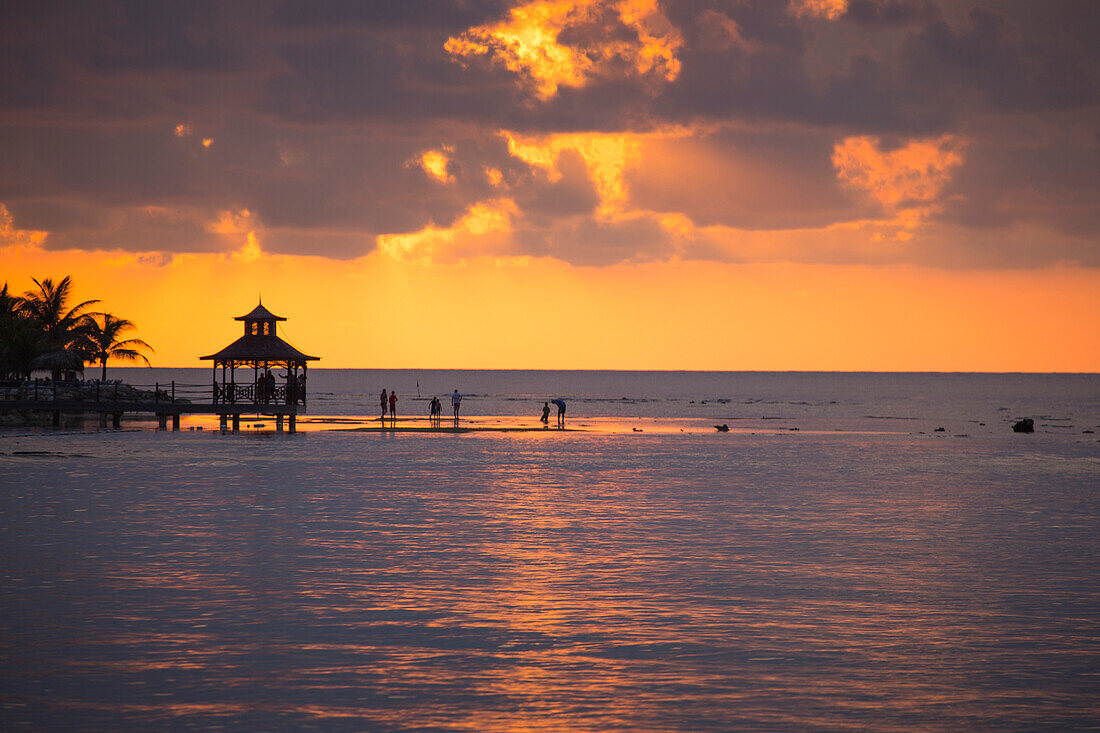 Silhouette of people in shallow water and pavillion on jetty at sunset Rose Hall, near Montego Bay, Saint James, Jamaica