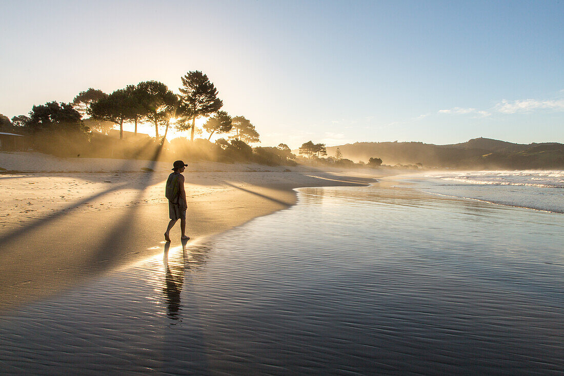 Whangapoua Beach, Sandstrand, Sonnenuntergang, Gegenlicht, Brandung, Ebbe, Silhouette, junge Frau wandert am Strand, Coromandel, Nordinsel, Neuseeland