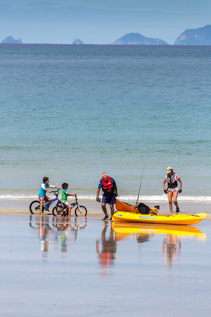 Sandstrand, Kinder mit Fahrrädern am Strand, Paar, Menschen mit Kajak und Angel, Gelb, Sommer, Urlaub, Nordinsel, Neuseeland