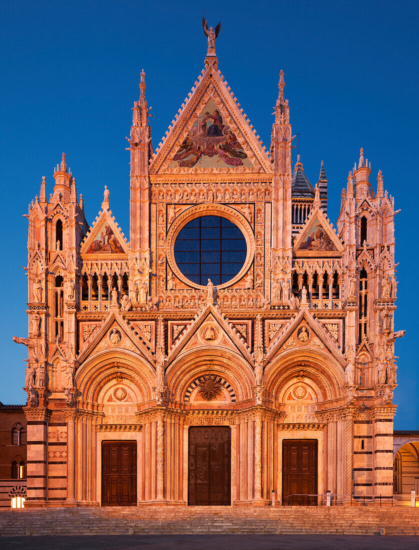 Facade of the cathedral Cattedrale di Santa Maria Assunta in Siena with the Porte, round glass windows and frescoes in the blue hour, Tuscany, Italy