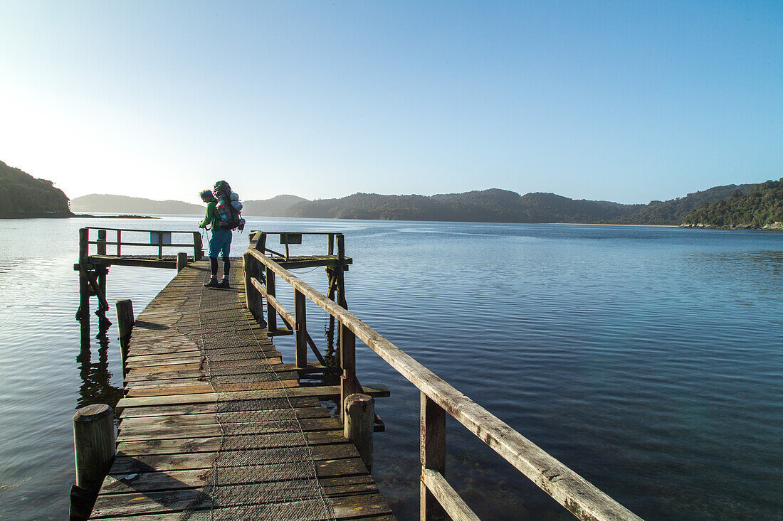 tramper with backpack, water taxi pick up point, jetty, wilderness, Stewart Island, Rakiura, New Zealand