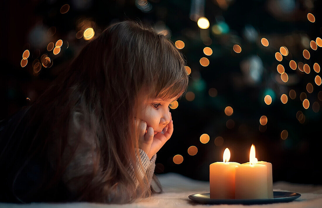 Caucasian girl laying on floor watching burning candles