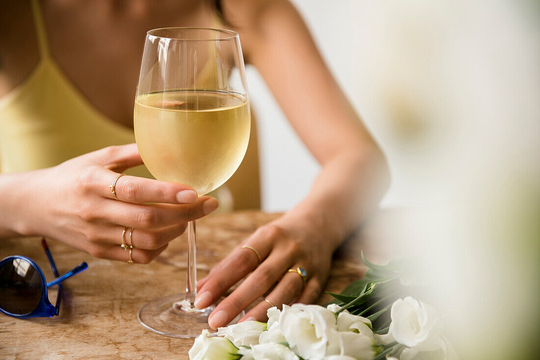 Hispanic woman drinking wine near flowers and sunglasses