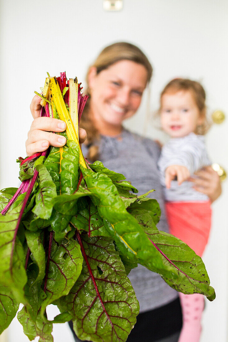 Smiling Caucasian mother holding daughter showing lettuce