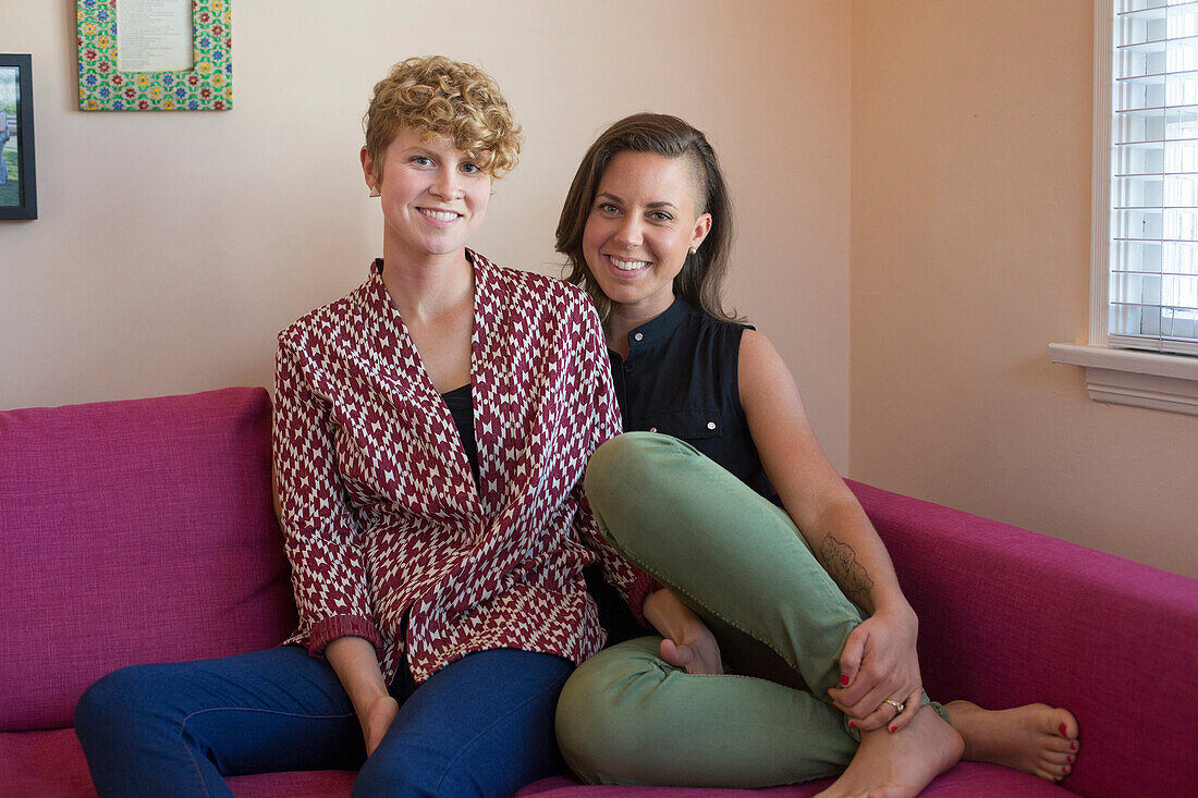 Caucasian lesbian couple smiling on sofa