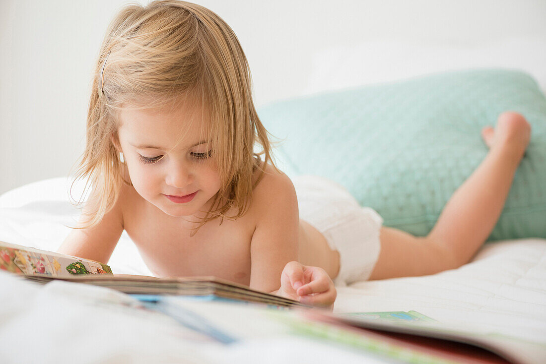 Caucasian girl reading book on bed