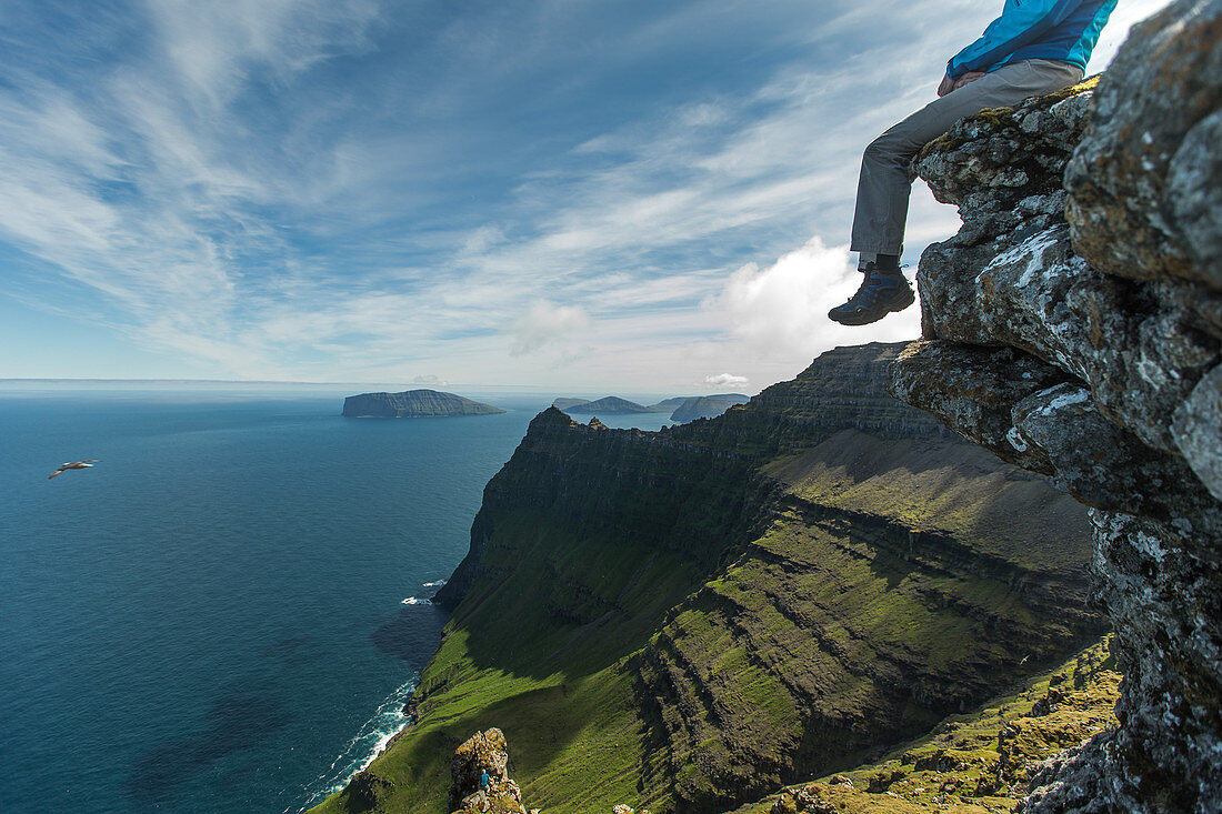 Man sitting on the edge of a cliff  from a mountain at the sea, Faeroe Islands