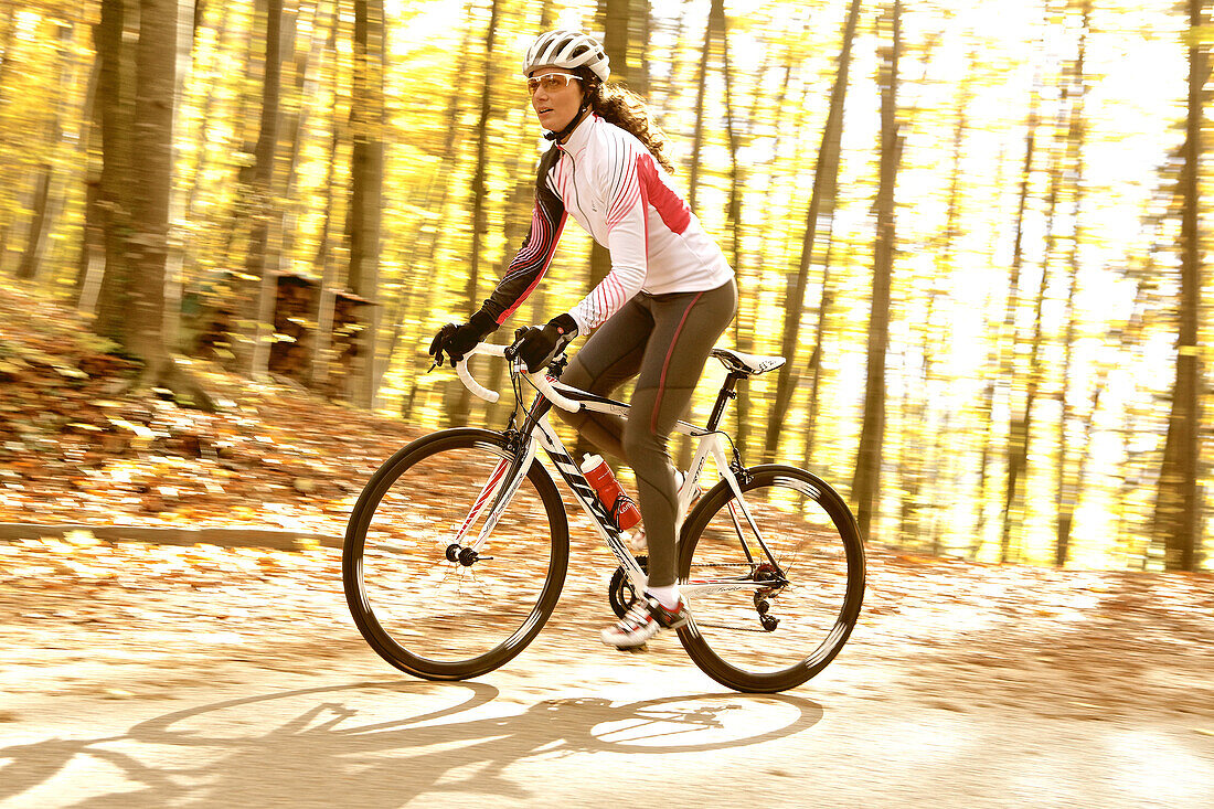 Young woman riding with her bike on a street at a forest, Fuessen, Bavaria, Germany
