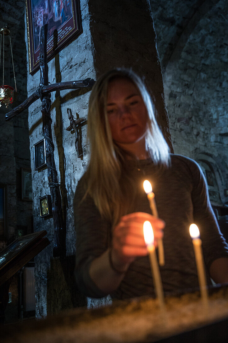 Young woman lighting a candle in a small church, Gudauri, Mtskheta-Mtianeti, Georgia