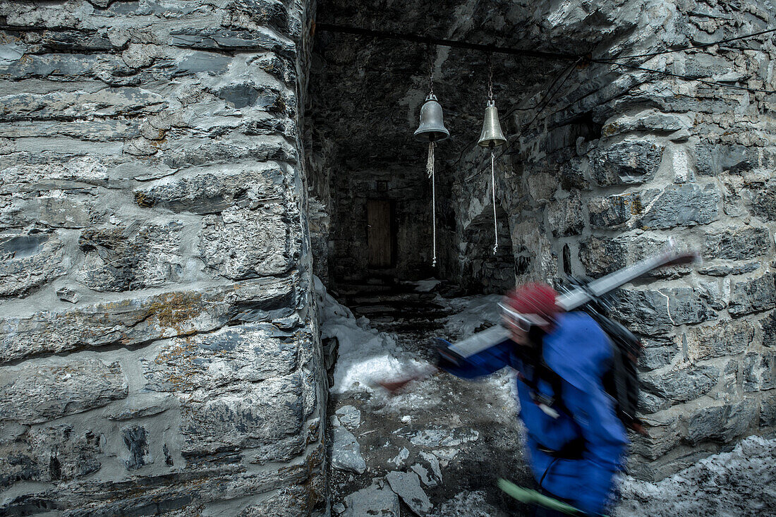 Female skier walking past small bells of a ruin, Gudauri, Mtskheta-Mtianeti, Georgia