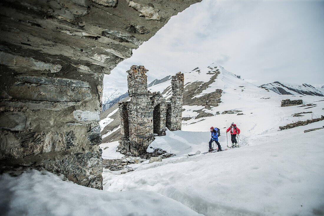 Zwei junge Skifahrer laufen an einer Ruine in den Bergen vorbei, Gudauri, Mzcheta-Mtianeti, Georgien