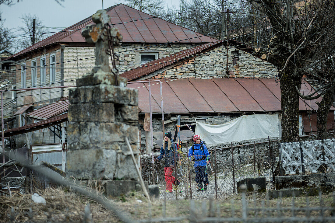 Two young female skiers wakling through a village, Gudauri, Mtskheta-Mtianeti, Georgia