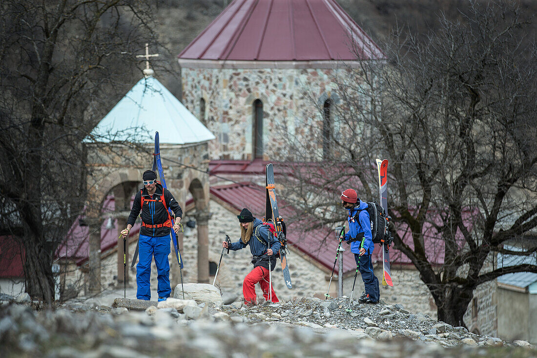 Drei junge Skifahrer laufen an einer Kirche in einem Dorf vorbei, Gudauri, Mzcheta-Mtianeti, Georgien