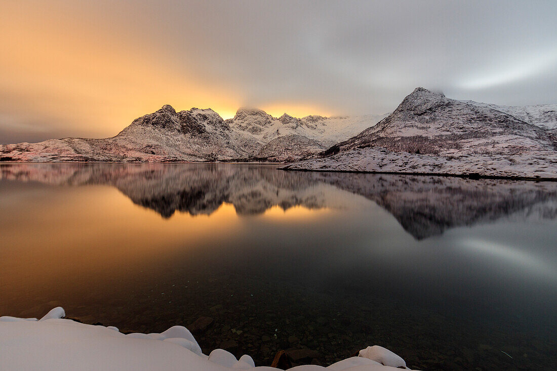 Das Licht des Mondes und der schneebedeckten Gipfel spiegelt sich in der kalten See beleuchtet die Nacht in Svolvaer, Lofoten, Arktis, Norwegen, Skandinavien, Europa