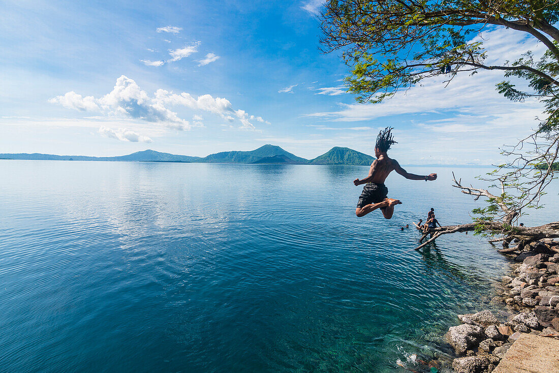 Mann springt in die Bucht von Rabaul mit Vulkan Tavurvur im Hintergrund, Ost-Neuen Britannien, Papua-Neuguinea, Pazifik