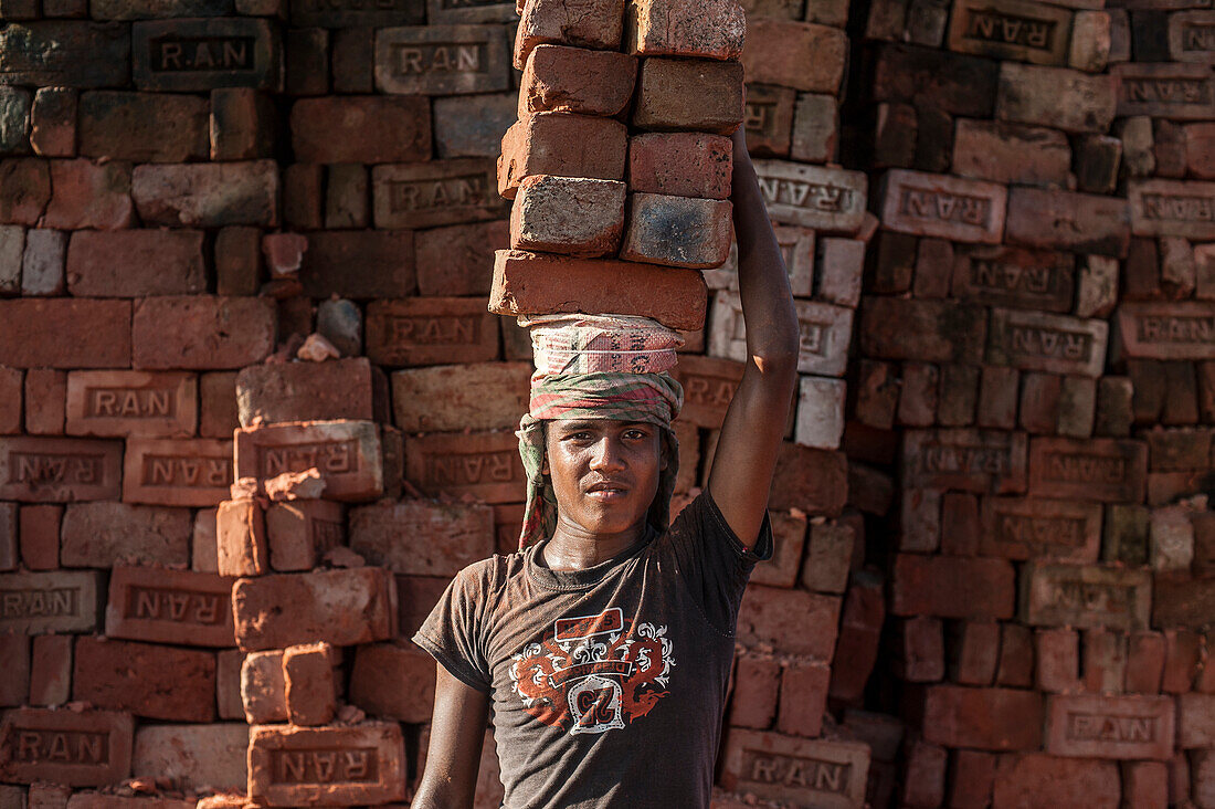 A young man carries up to 50 kilos of bricks by balancing them on his head, brick factory in Chittagong Hill Tracts, Bangladesh, Asia