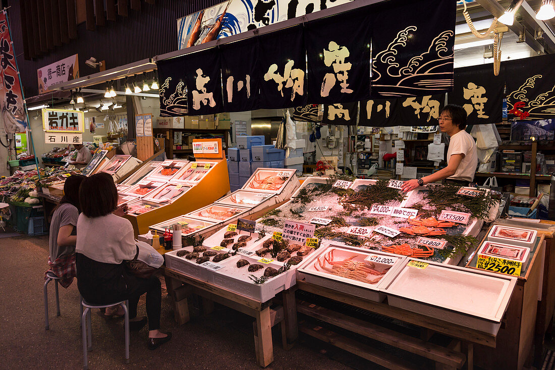 Diners sit and talk to seafood stall owner, Omicho fresh food market, network of covered stall lined streets, Kanazawa, Japan, Asia