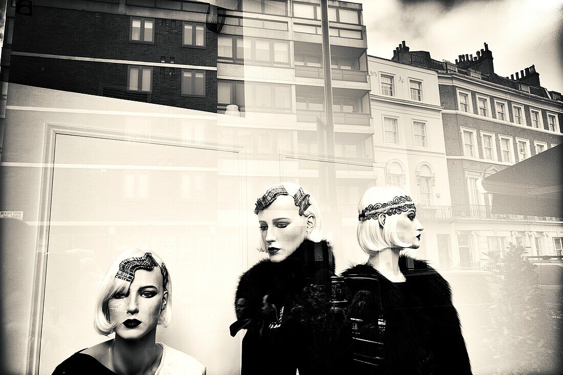 Fashion store, show window. Three female mannequins with elegant clothes, hairstyles and make up. Reflections on glass. London, England