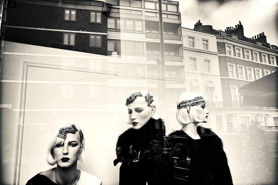Modegeschäft, Schaufenster. Drei weibliche Schaufensterpuppen mit eleganten Kleidern, Frisuren und Make-up. Reflexionen auf Glas. London, England