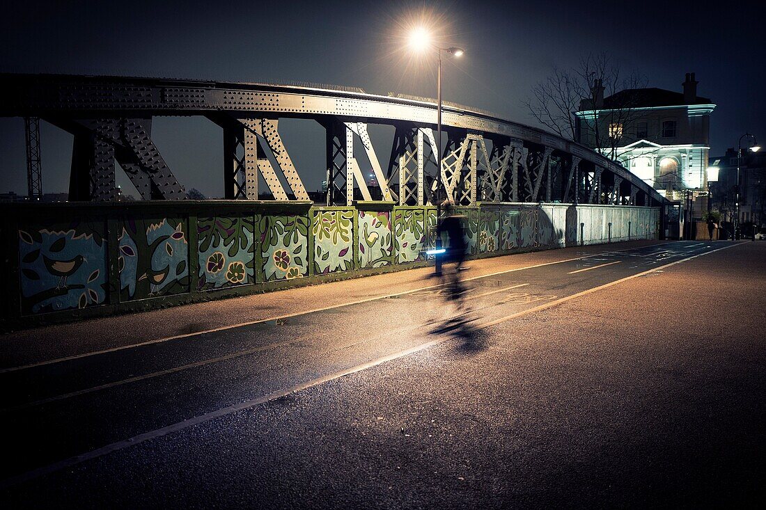 Iron bridge and biker, with street lamp. Blurred motion. Regent's Park Rd. London, England