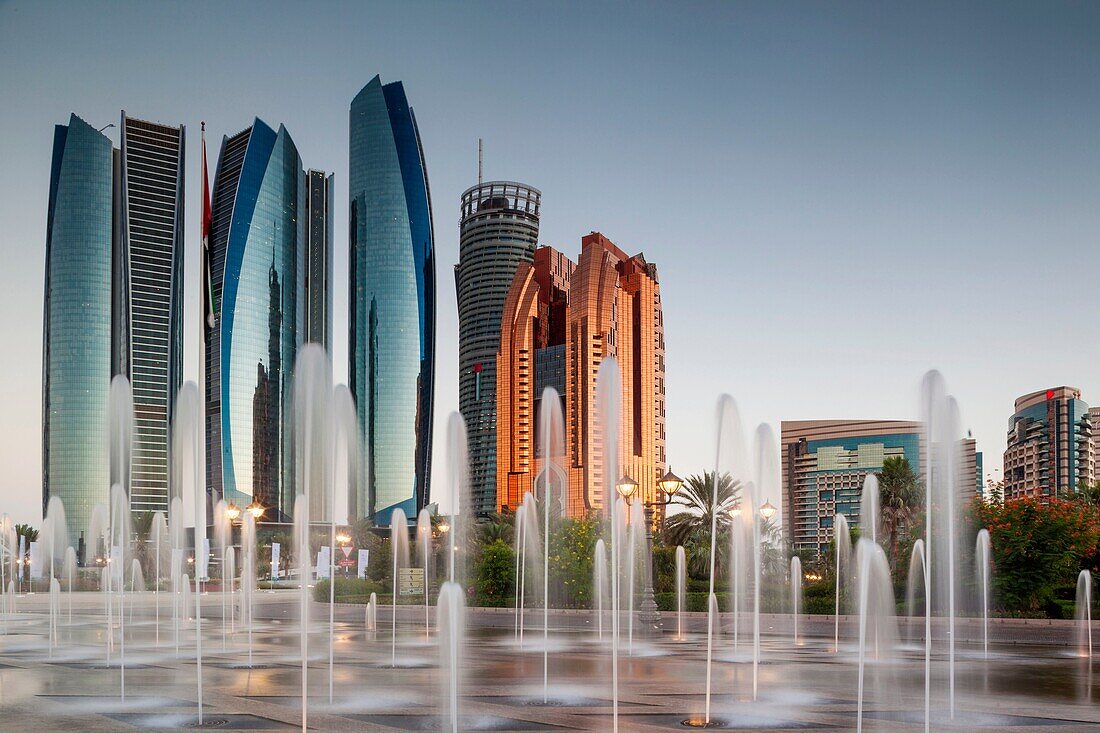 UAE, Abu Dhabi, Etihad Towers and Emirates Palace Hotel fountains, dusk.