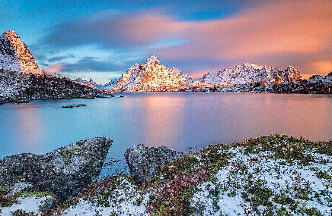 The pink sky at sunrise illuminates Reine village with its cold sea and the snowy peaks. Lofoten Islands Northern Norway Europe.